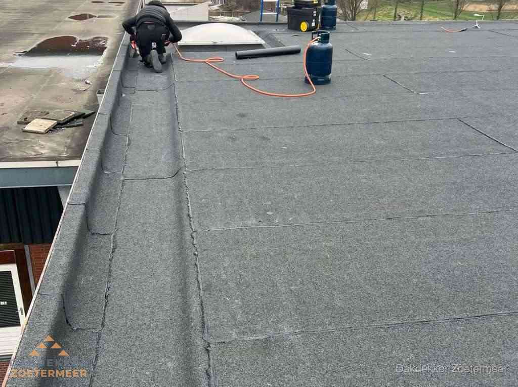 Dakdekker repareert bitumen dakbedekking op groot plat dak in Zoetermeer